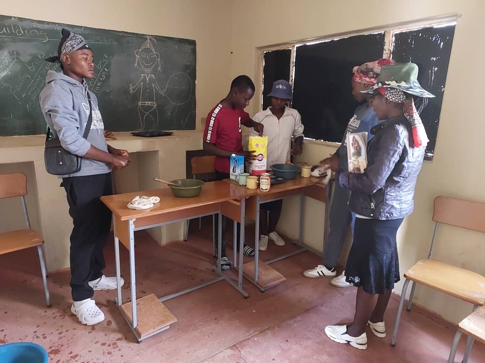 Trainees prepare food on tables in a classroom during a baking class.