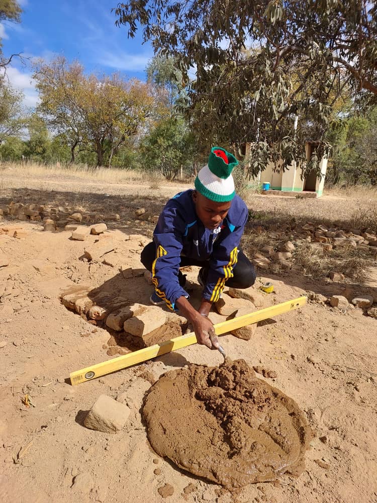 A trainee lays bricks, checking them with a spirit level, during a building class.