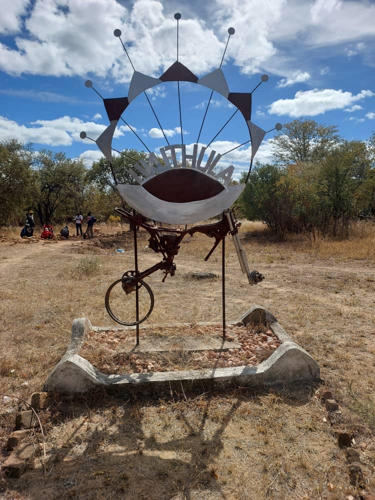 A tall metal sculpture with radiating spokes stands in the dry grounds of the Enyandeni Training Centre.