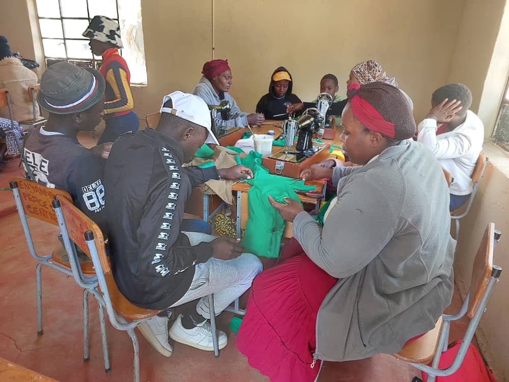 Trainees sit around a table sewing green fabric for school uniforms.
