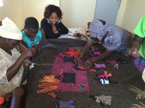 Women sit around a table making a textile artwork together from cut-out pieces of fabric.