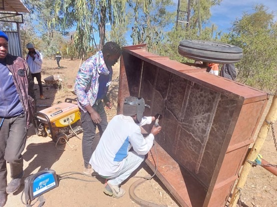 A trainee welds a large metal frame outdoors during a welding class.