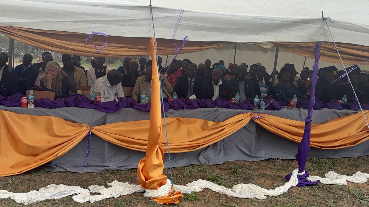 Guests seated along a head table dressed in purple and gold under a large white marquee.