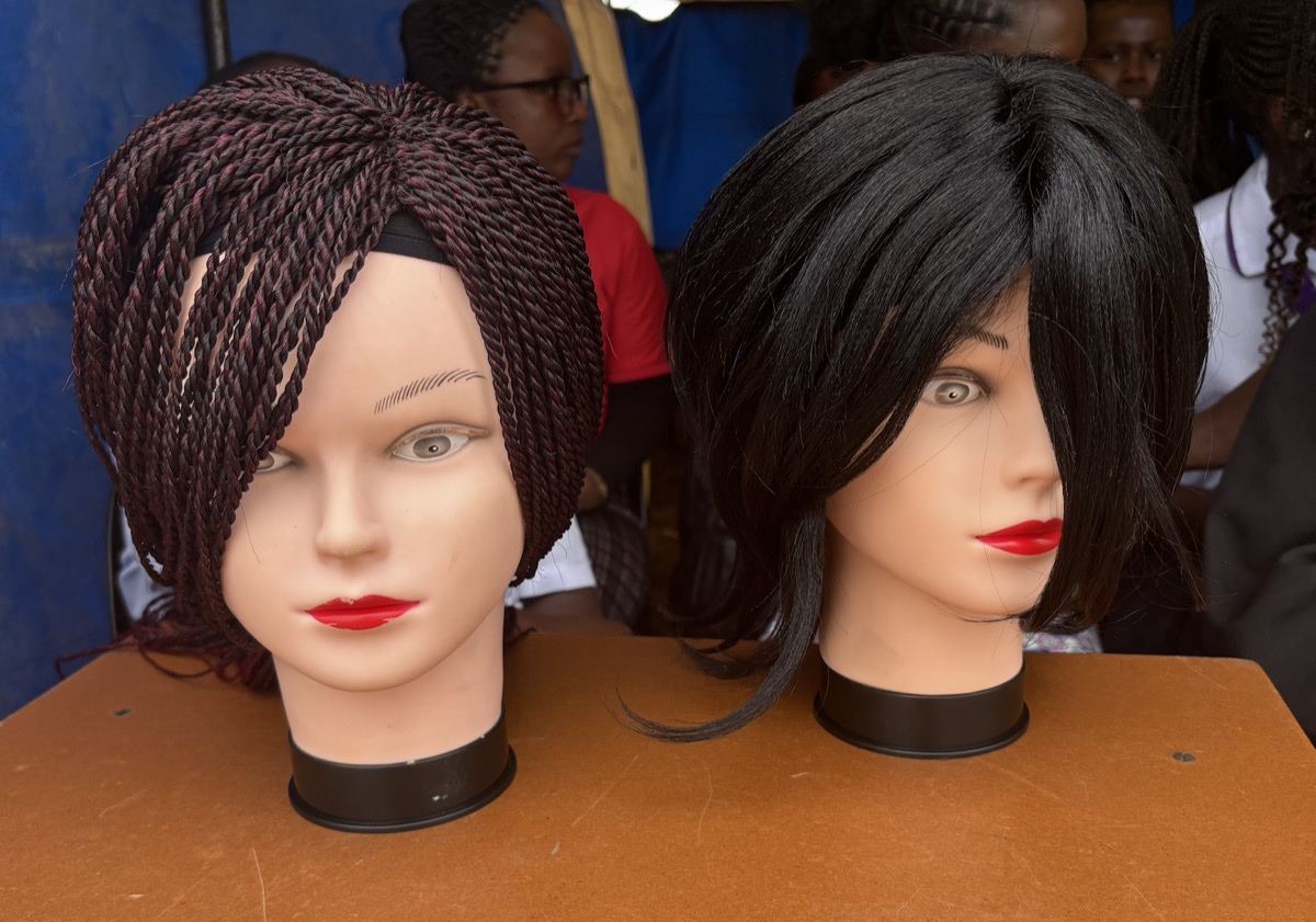 Two mannequin heads on a table, one wearing a braided wig and one a straight black wig.